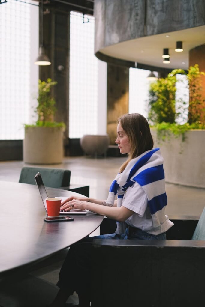 A woman in a modern office working on her laptop with a coffee cup nearby.